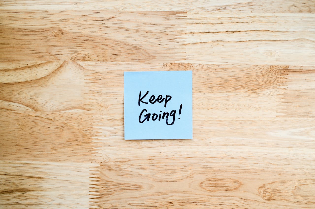 Light stained table top with blue note in the centre with the words 'Keep Going!'