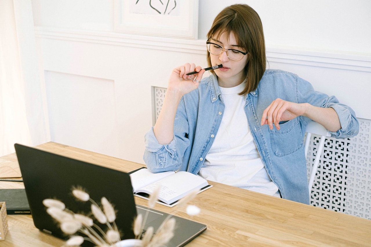 Woman with pen to lips contemplating empty notebook